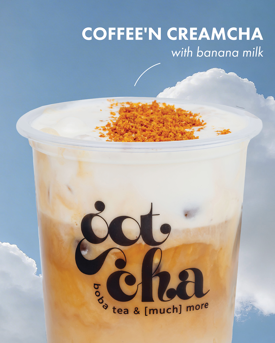 Close-up of iced coffee creamcha with banana milk topping and brown crumbles on top in a clear cup.