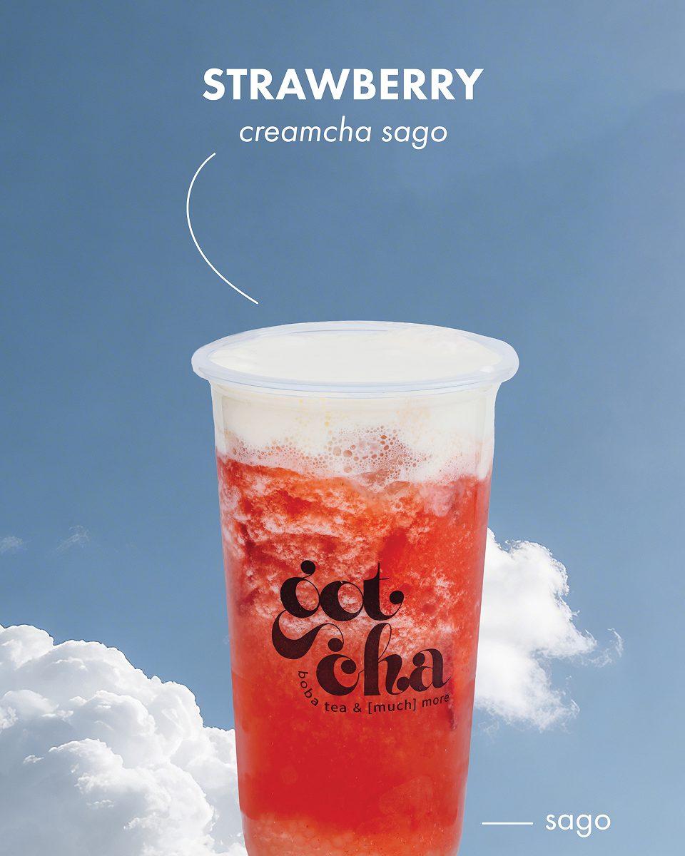 Strawberry creamcha sago drink in a clear cup with a blue sky and clouds background.